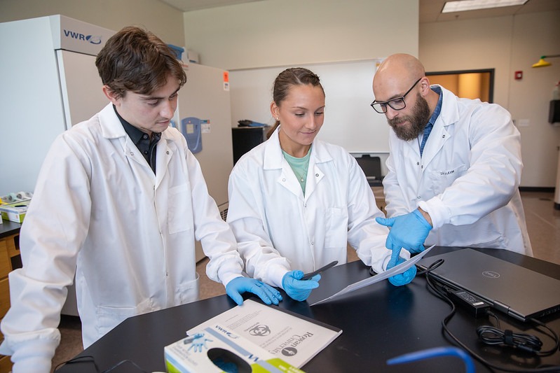 A group of three Rowan University student and staff in the master's in nursing degree program work together in a healthcare setting, looking at a document. 