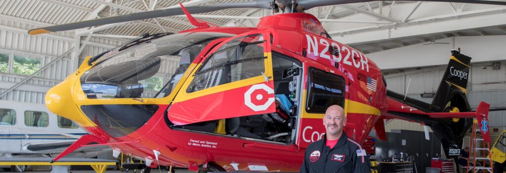 Rowan University master of science in nursing student who is a flight nurse stands next to a red Cooper medical helicopter.