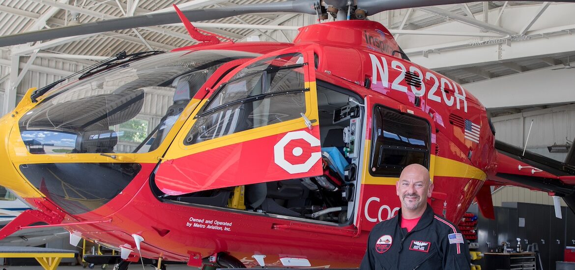 Rowan University master of science in nursing student who is a flight nurse stands next to a red Cooper medical helicopter.