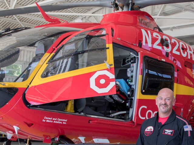 Rowan University master of science in nursing student who is a flight nurse stands next to a red Cooper medical helicopter.