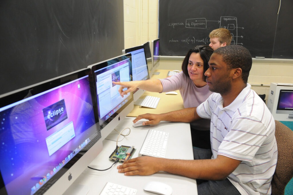 Supervisor mentoring an employee who graduated with a computer technology degree and is now a computer systems analyst