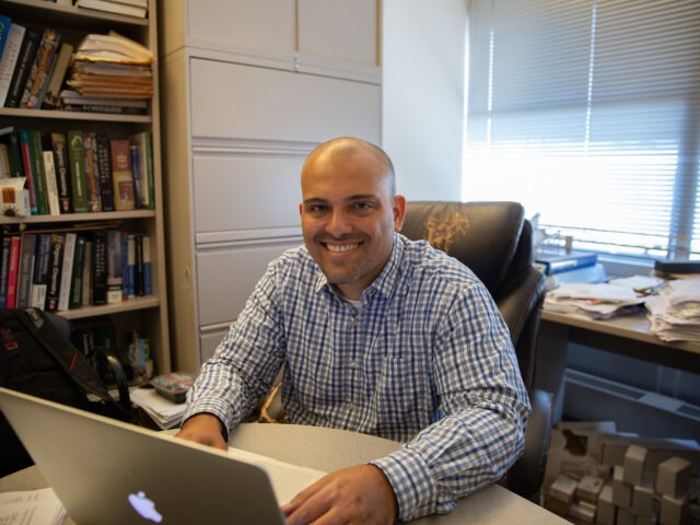 A university professor working on a laptop in his office, illustrating the dynamic and interactive experience of an online doctorate in education