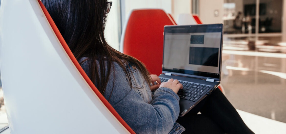 Student earning a bachelor’s degree in respiratory therapy online, studying on a laptop in a modern lounge