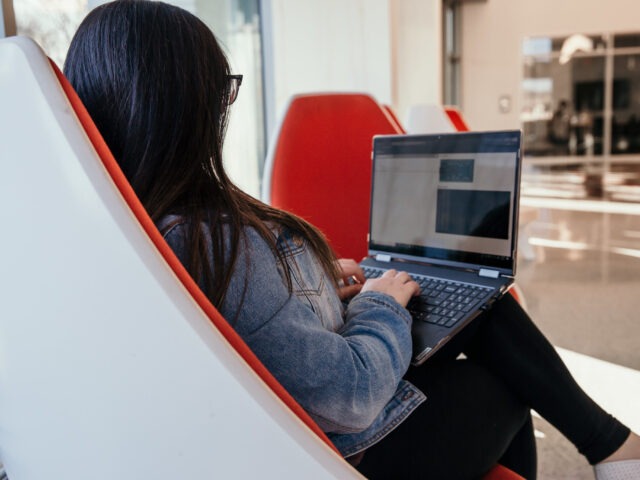 Student earning a bachelor’s degree in respiratory therapy online, studying on a laptop in a modern lounge