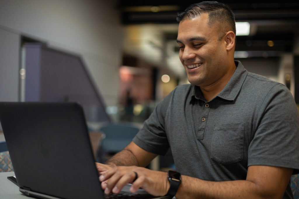 Smiling adult student working on an online computer technology degree from a laptop in a flexible learning environment