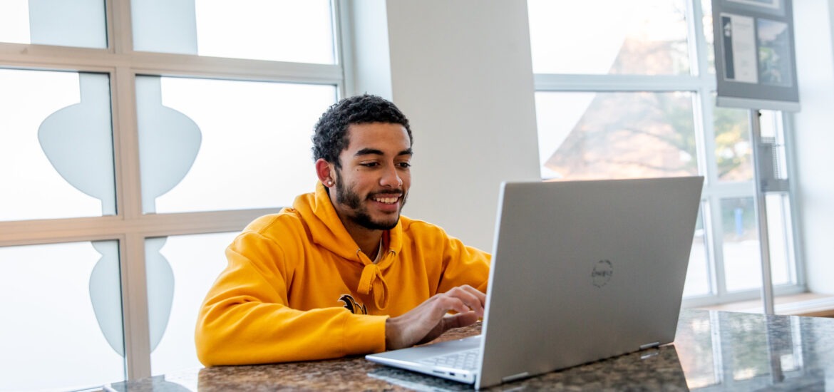 Male student sitting on laptop doing coursework for online criminology degree