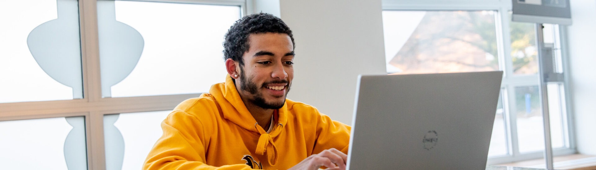 Male student sitting on laptop doing coursework for online criminology degree.