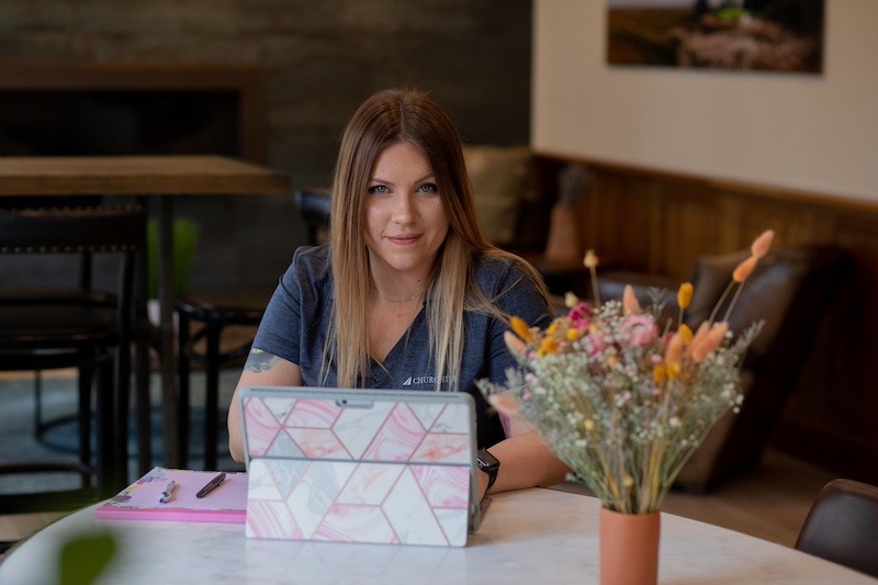 A Rowan University student sits at a kitchen table at home working on a laptop next to a vase of flowers.