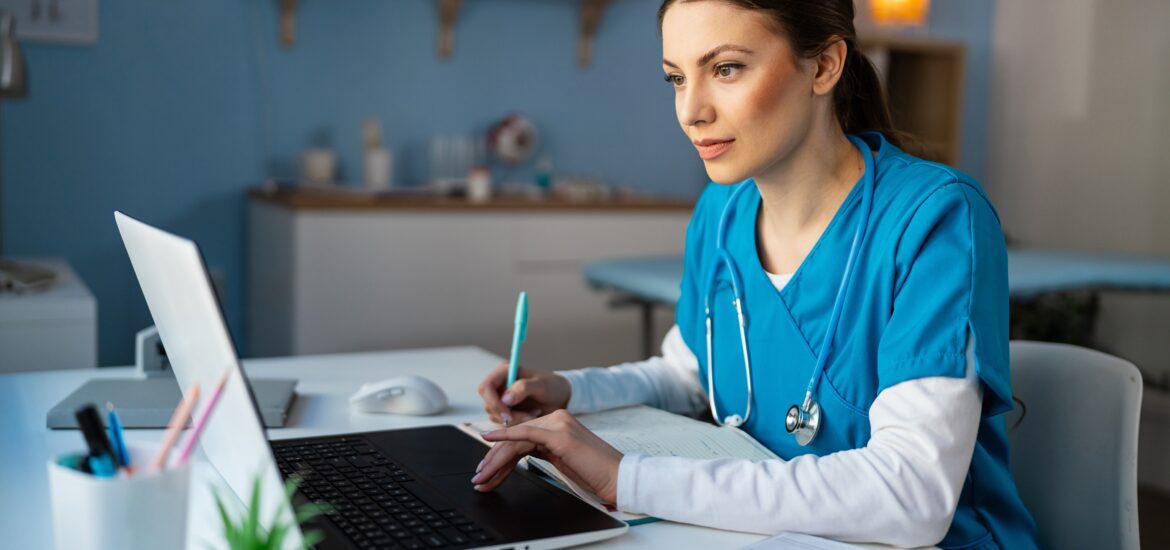 Student sitting at a table in scrubs completing coursework for a bachelor’s degree in respiratory therapy.