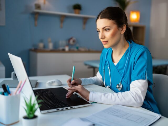 Student sitting at a table in scrubs completing coursework for a bachelor’s degree in respiratory therapy.
