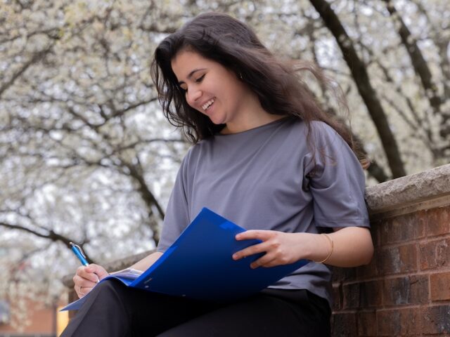 A Master's in Psychiatric Mental Health Nurse Practitioner student at Rowan University sits outside studying, with a flowering tree behind her.