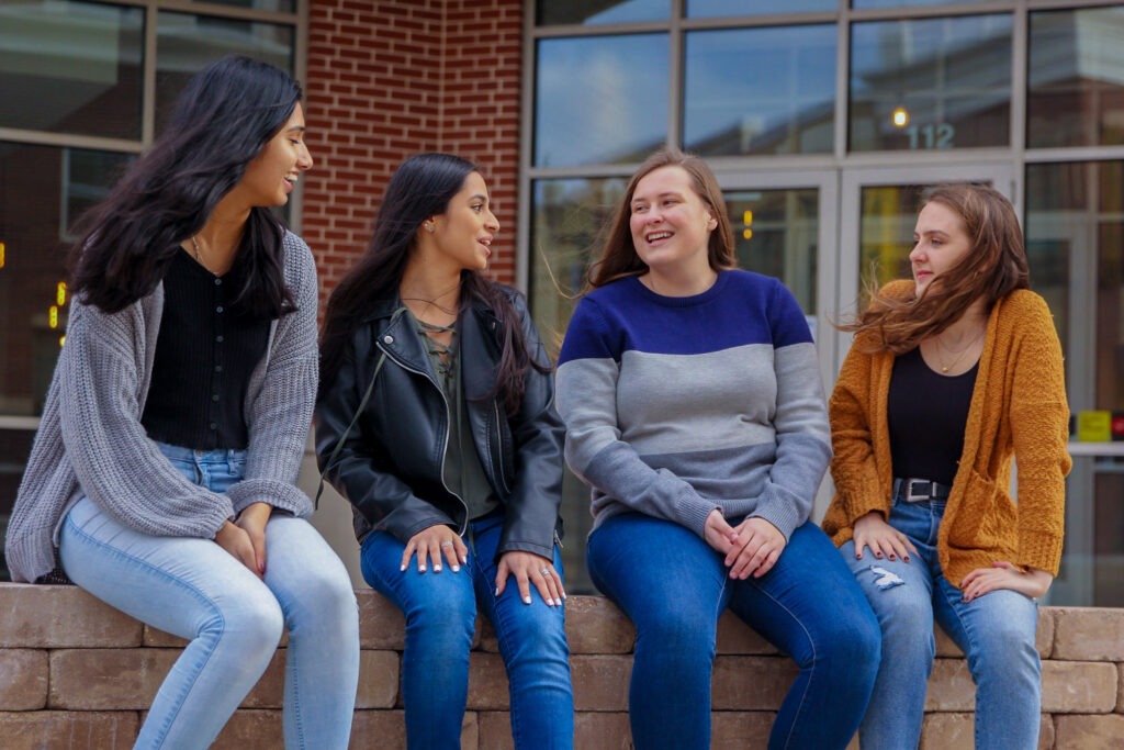 Four Rowan University friends laughing, sitting together outside a building.