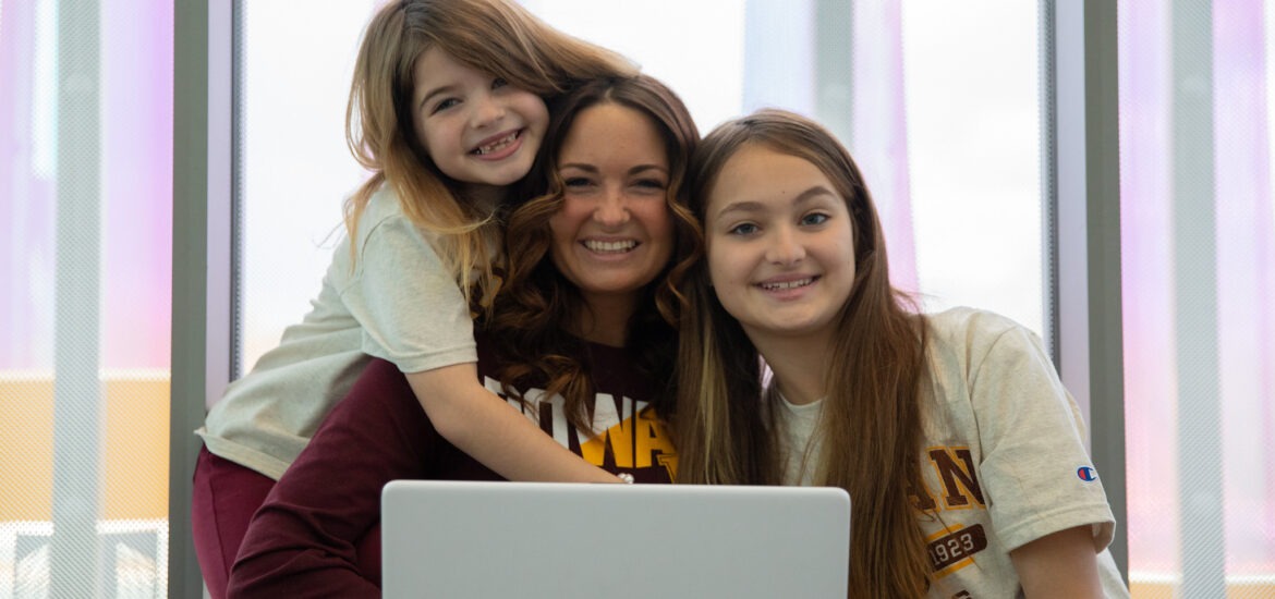 Smiling Rowan student in online class with two daughters by her side