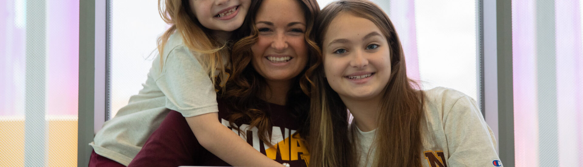 Smiling Rowan student in online class with two daughters by her side.