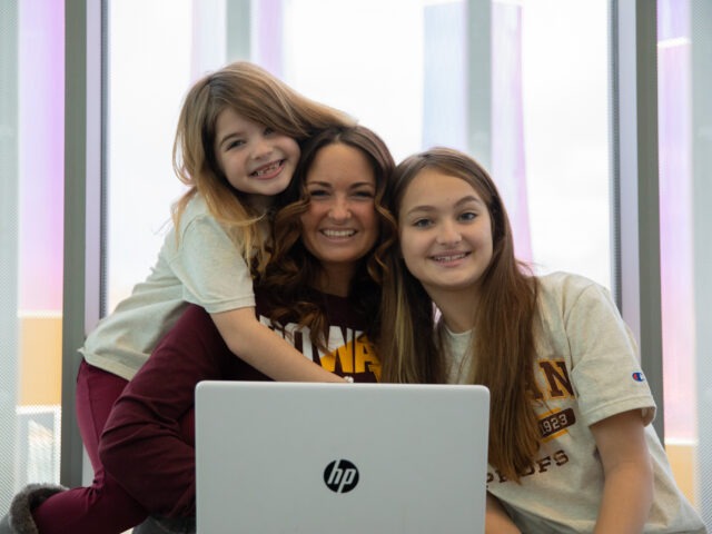 Smiling Rowan student in online class with two daughters by her side