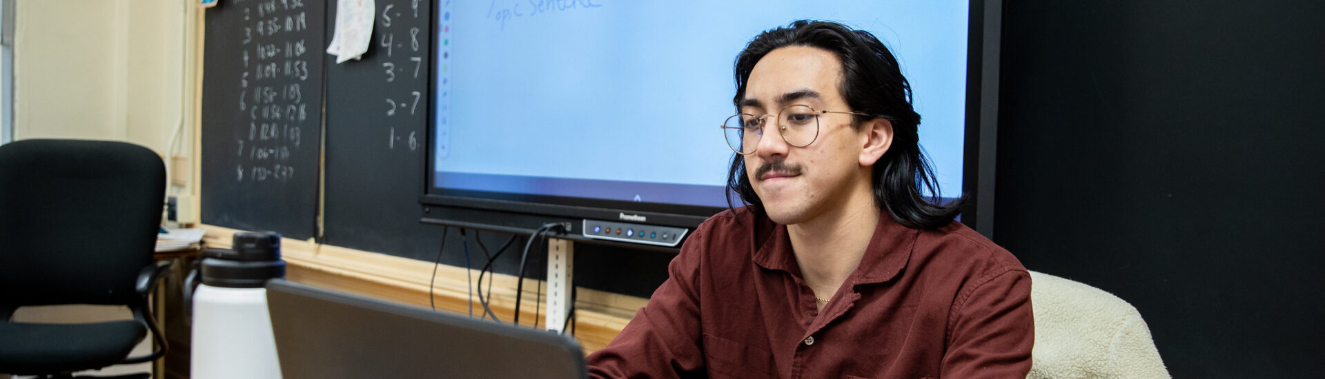 Teacher working on laptop during lunch break in classroom, advancing career through online supervisor certification program.