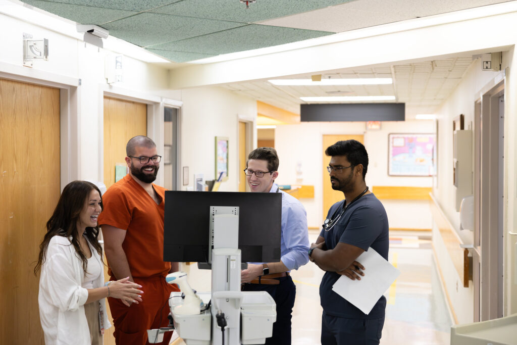 A physician stands with healthcare workers in a hall around a mobile work station.