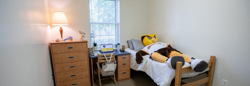 The Rowan mascot owl lays on a bed in a dorm.