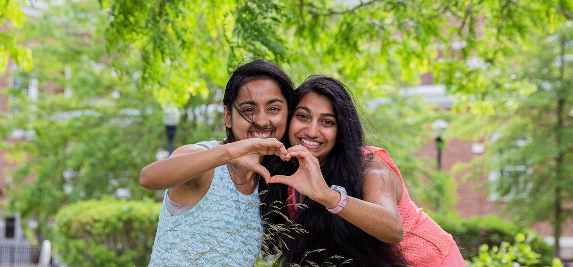Two best friends at Rowan University create the shape of a heart by each of them holding their hand to be one side of it.