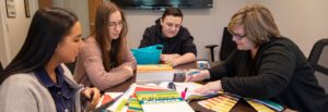 Students and Rowan University advertising faculty sit together at. a table working.