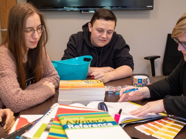 Students and Rowan University advertising faculty sit together at. a table working.
