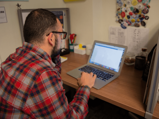 A Rowan University bilingual teacher certificate student works on his laptop in his home office.