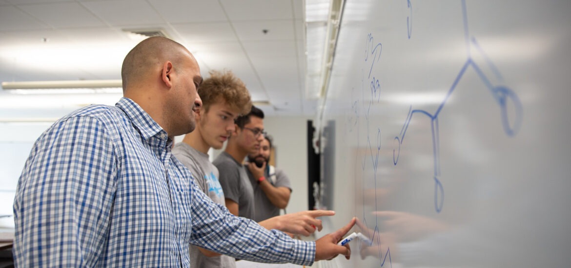 Educator guiding students through a lesson at the whiteboard, showing real-world applications of teacher leadership