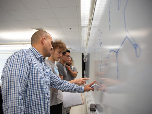 Educator guiding students through a lesson at the whiteboard, showing real-world applications of teacher leadership