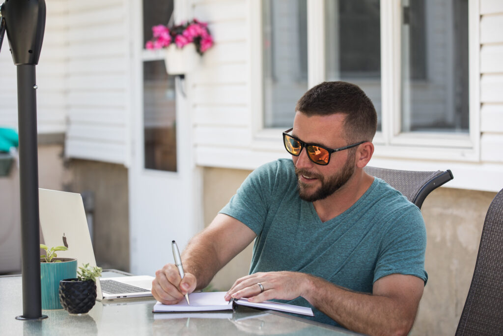 Man studying outdoors with a laptop and notebook, showing the flexibility of learning from anywhere in an online graduate program