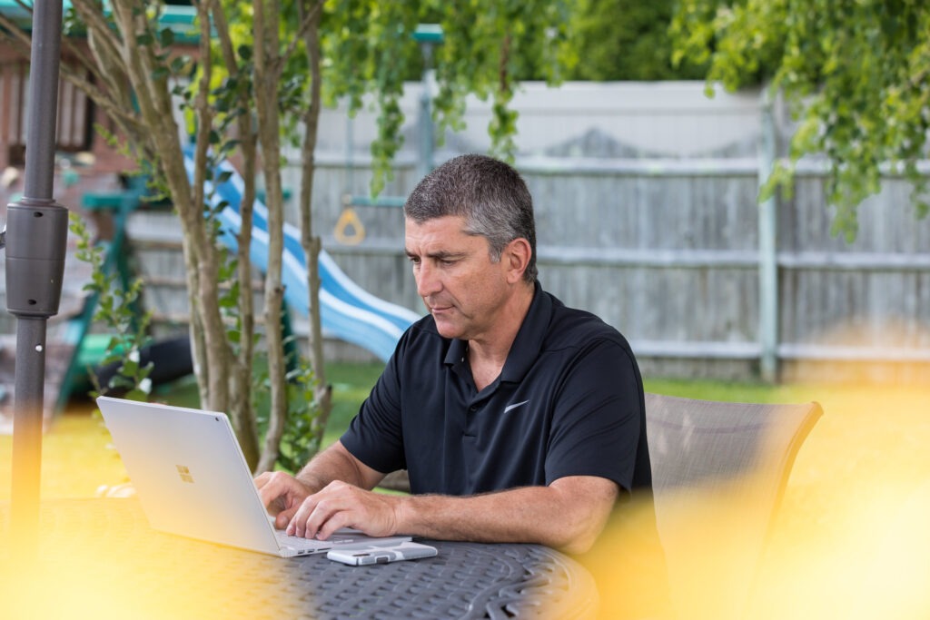 Middle-aged man working remotely on a laptop in his backyard, highlighting the remote work opportunities with an online MBA