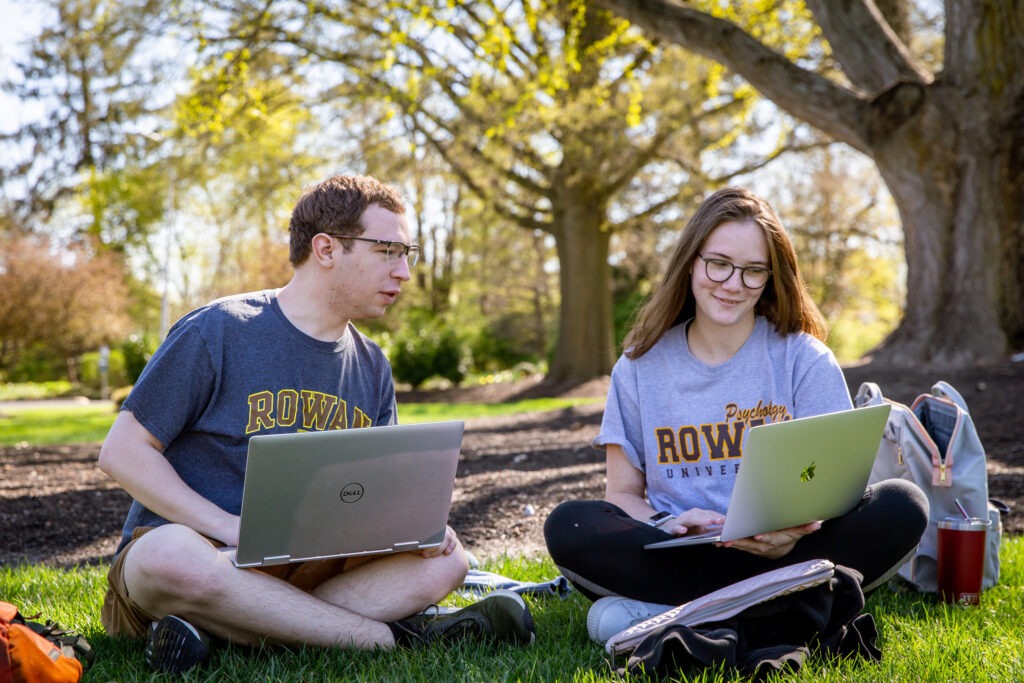 Two Rowan University students studying outdoors on laptops, representing the flexibility and accessibility of Rowan’s online graduate programs