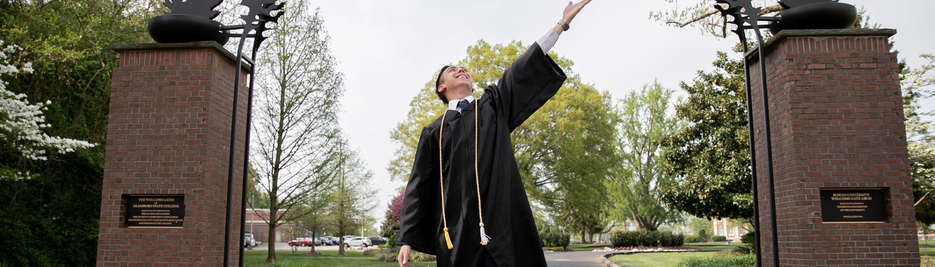 Graduating Rowan University online student standing confidently under the Rowan arch.