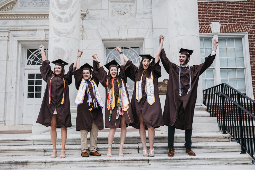 Group of college graduates in caps and gowns holding hands and cheering on graduation day, celebrating the excitement of commencement and new beginnings