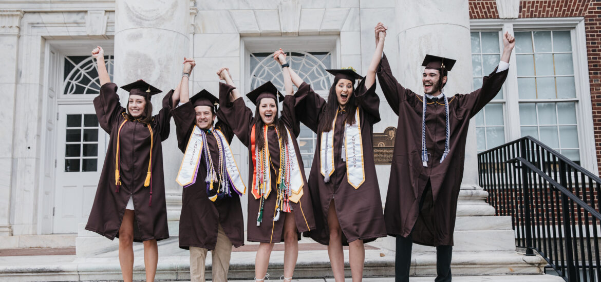 Group of college graduates in caps and gowns holding hands and cheering on graduation day, celebrating the excitement of commencement and new beginnings.