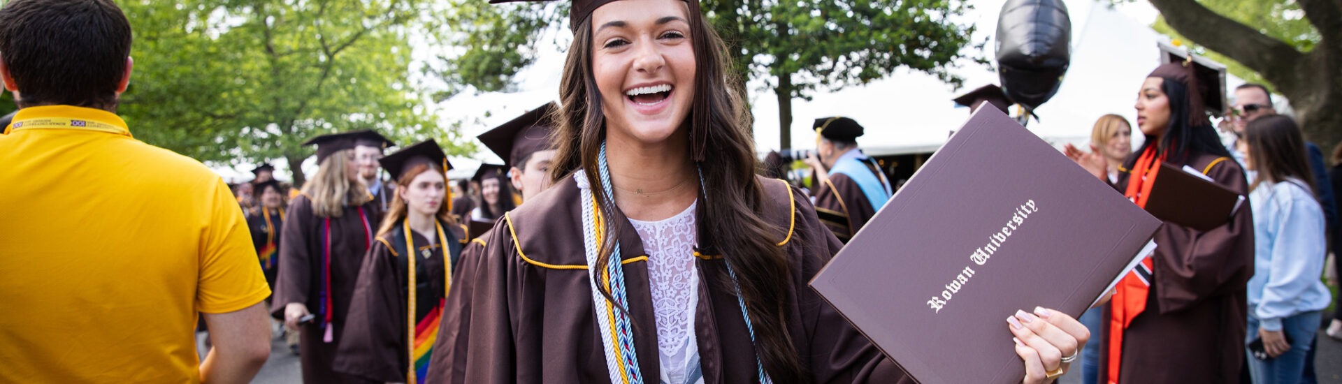 A smiling Rowan University graduate holds her diploma during commencement, representing pride, accomplishment, and the start of a new chapter