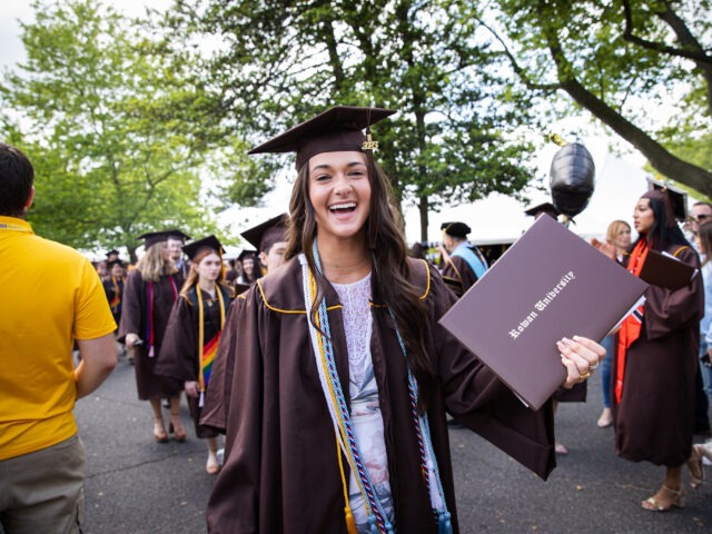 A smiling Rowan University graduate holds her diploma during commencement, representing pride, accomplishment, and the start of a new chapter