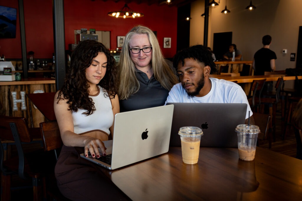 Three students collaborating with laptops in a café setting, illustrating the community and support available in Rowan’s online graduate programs