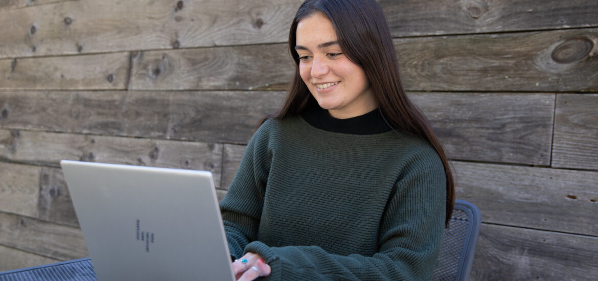 Student smiling while working on laptop outdoors, representing flexible learning in an online bachelor’s degree in criminal justice