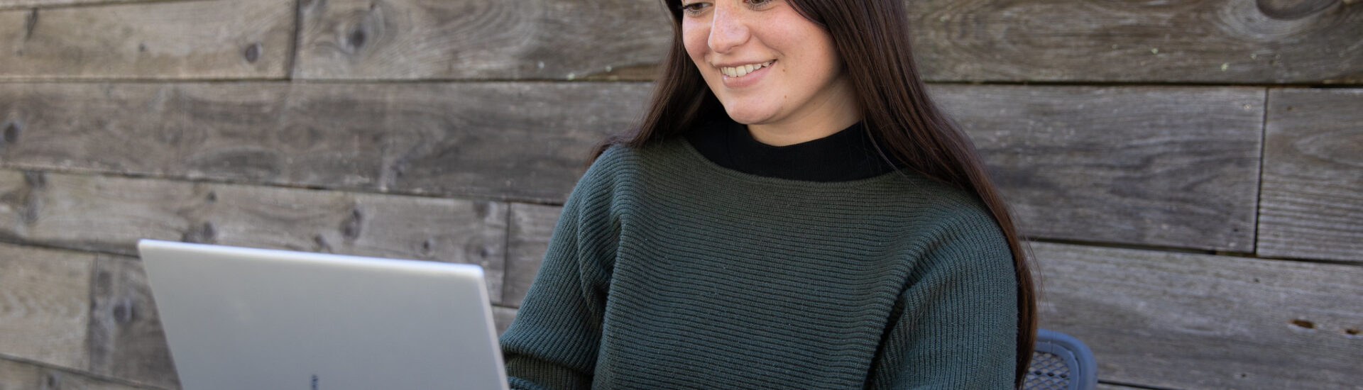 Student smiling while working on laptop outdoors, representing flexible learning in an online bachelor’s degree in criminal justice.