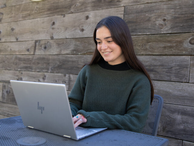 Student smiling while working on laptop outdoors, representing flexible learning in an online bachelor’s degree in criminal justice