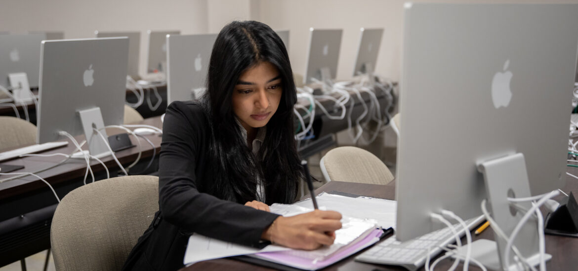 Student in computer lab taking notes while pursuing a cybersecurity masters online