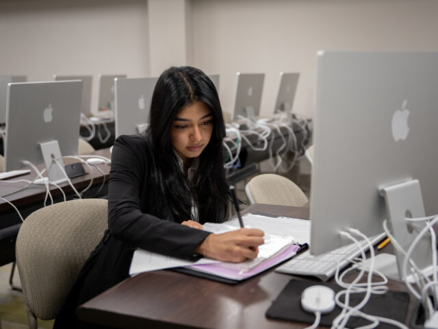 Student in computer lab taking notes while pursuing a cybersecurity masters online