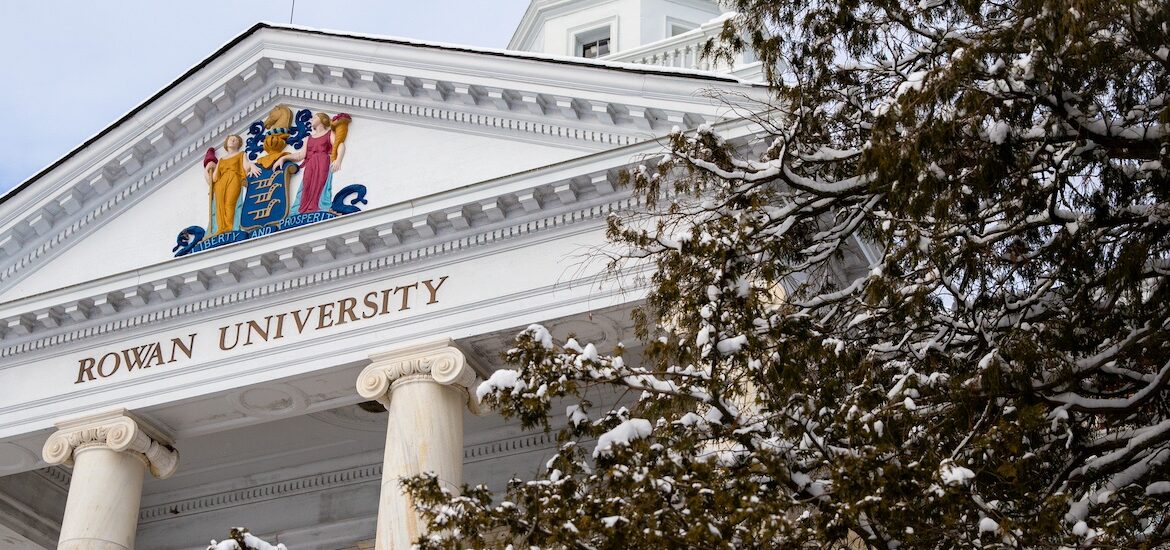An iconic look at the top of a classic college building on the campus of Rowan University, with a snowy tree peeking into view.