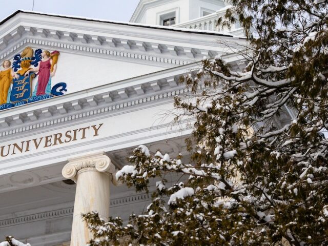 An iconic look at the top of a classic college building on the campus of Rowan University, with a snowy tree peeking into view.