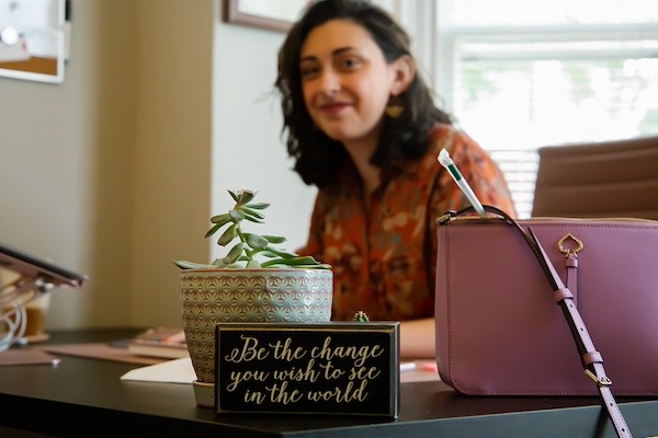 A Rowan master's in special education graduate sits at a desk blurred in the background, with a sign on her desk that reads "Be the change you wish to see in the world."