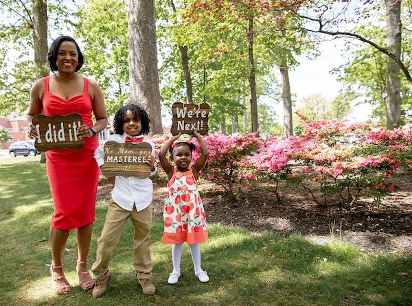 A Rowan master's in special education graduate holds a sign that says "I did it" and her two young children hold signs that say "No mom you mastered it" and "We're next!"