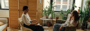 A therapist and a client sit facing each other, with plants around them, highlighting careers with a bachelors degree in psychology online.