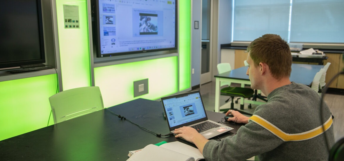 Student using laptop and smartboard in a tech-enabled classroom during a graduate program in educational technology