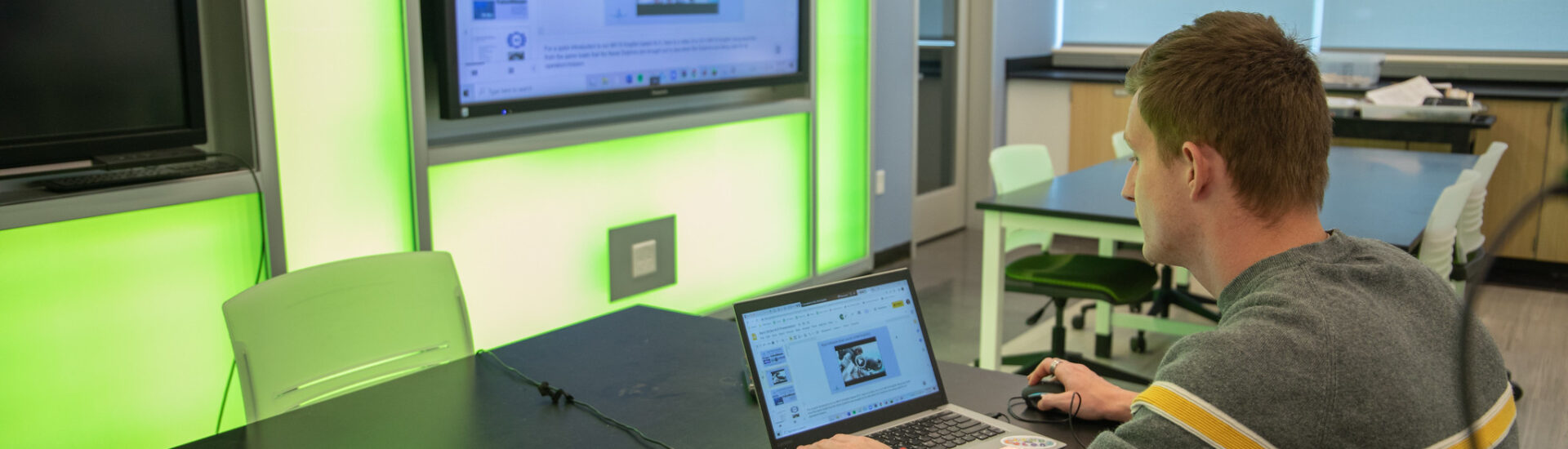 Student using laptop and smartboard in a tech-enabled classroom during a graduate program in educational technology.