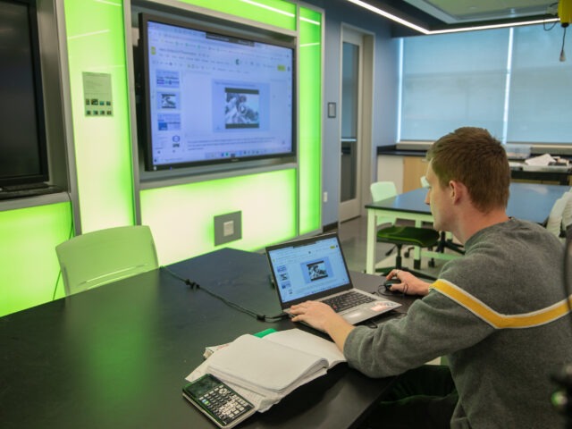 Student using laptop and smartboard in a tech-enabled classroom during a graduate program in educational technology